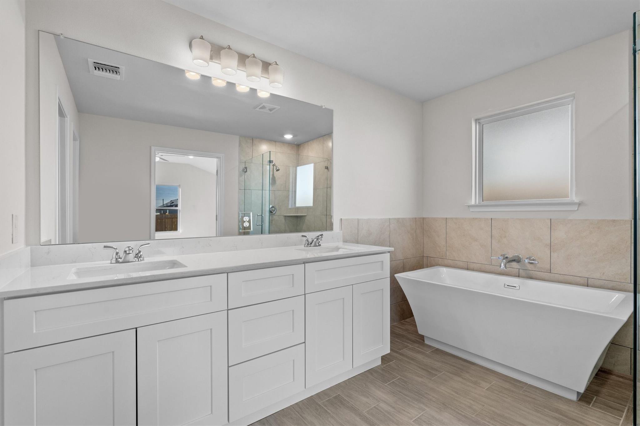 Bathroom with a double-sink vanity, glass shower, and freestanding soaking tub.