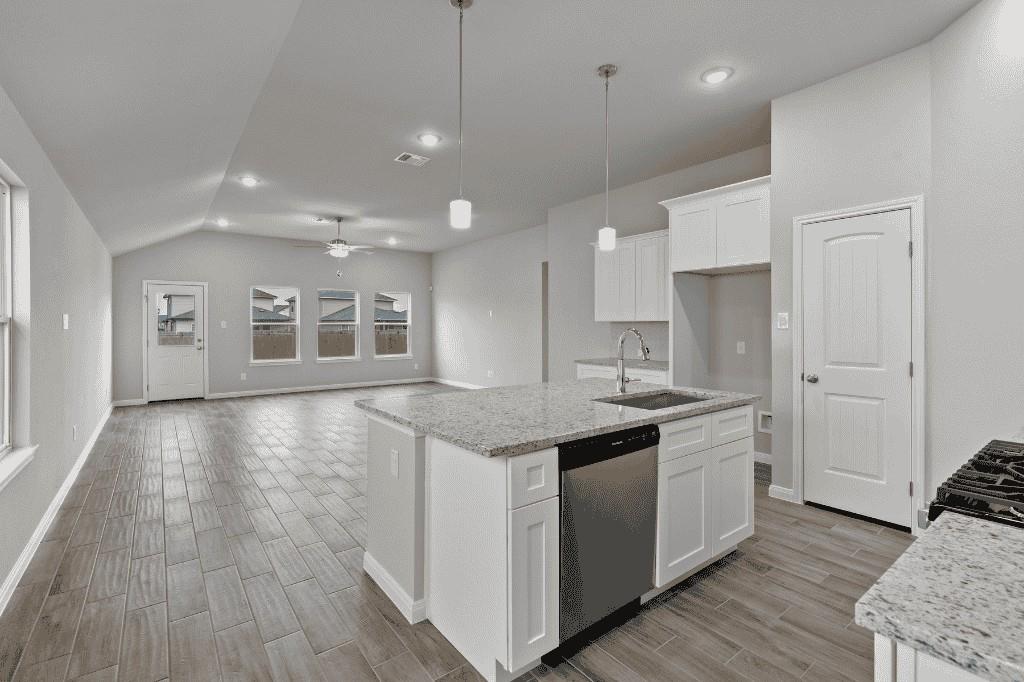 Vacant kitchen with a granite island, white cabinets, and gray tile flooring opening to a living area.