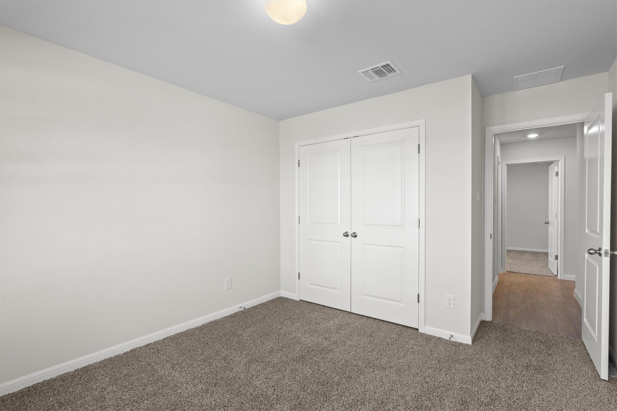 Empty carpeted bedroom with double closet doors and an open doorway to the hallway.
