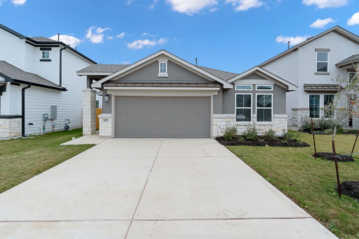 Gray single-story house with a two-car garage, stone accents, and a broad concrete driveway.