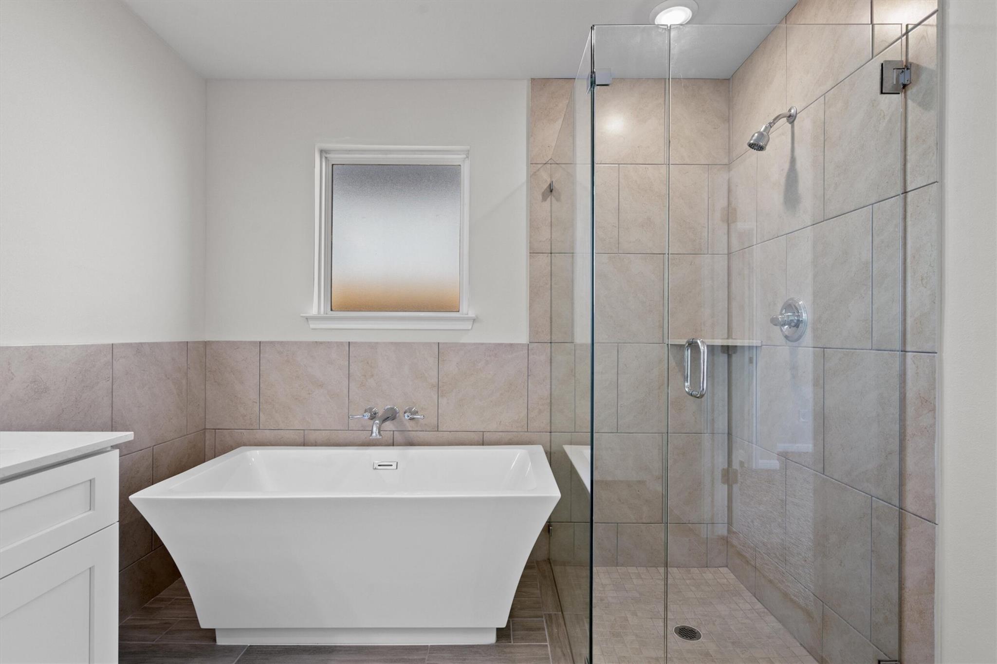 Bathroom with a freestanding tub, tiled walk-in shower, and frosted window.