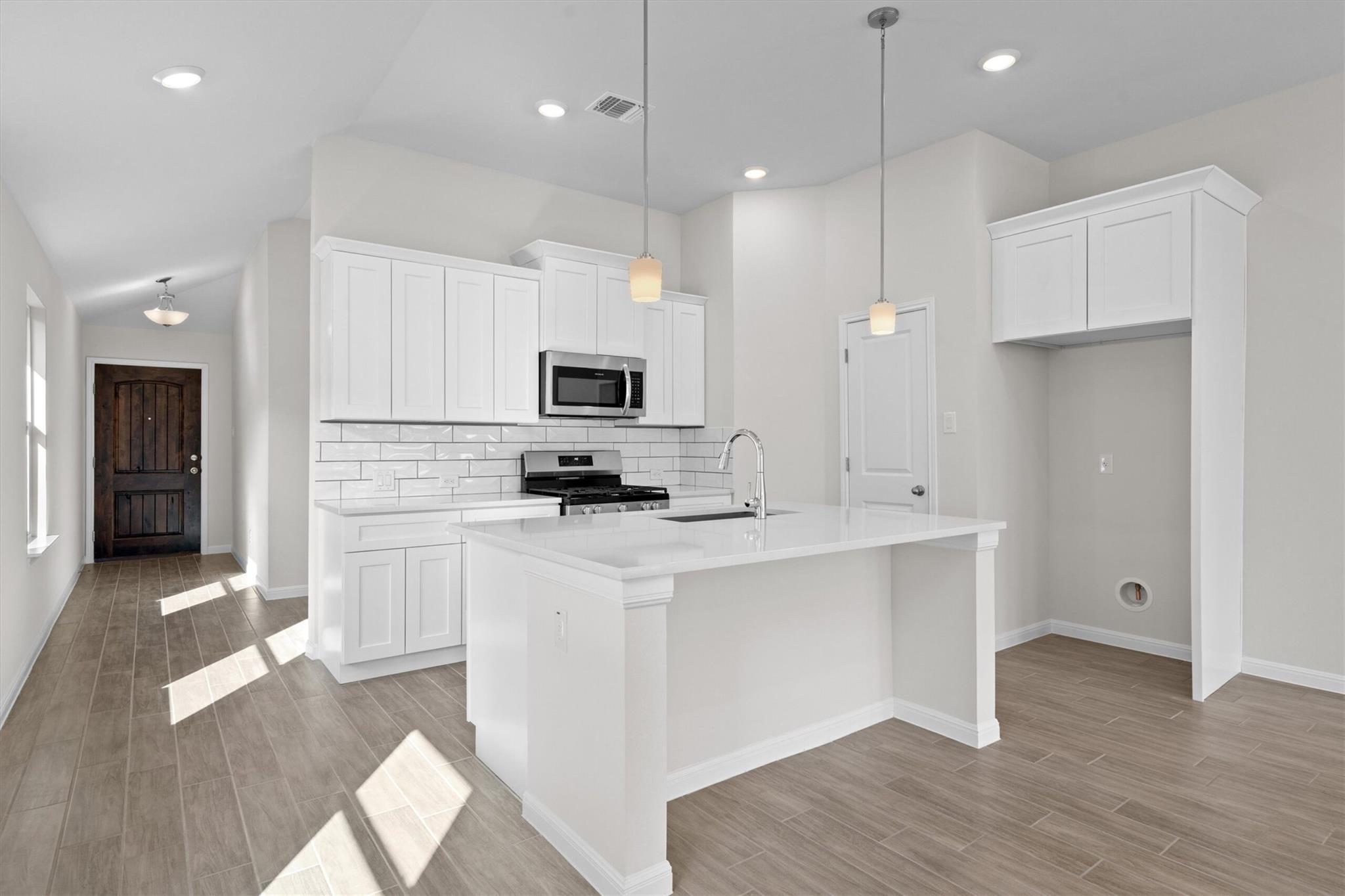 Unfurnished kitchen with a large white island, shaker cabinets, subway tile backsplash, and stainless steel appliances.