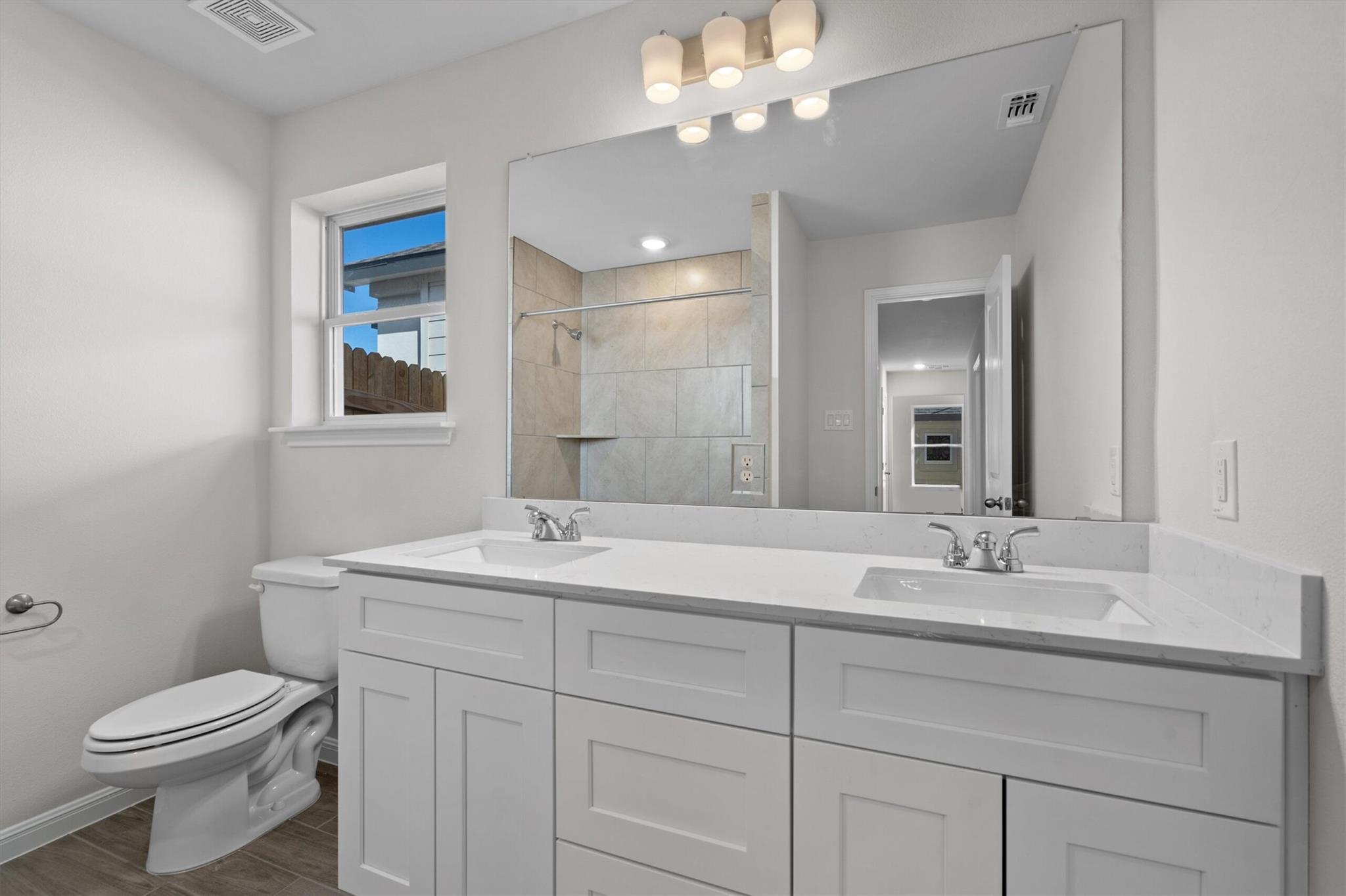 Bathroom with a double-sink vanity, large mirror, tiled shower, and window.