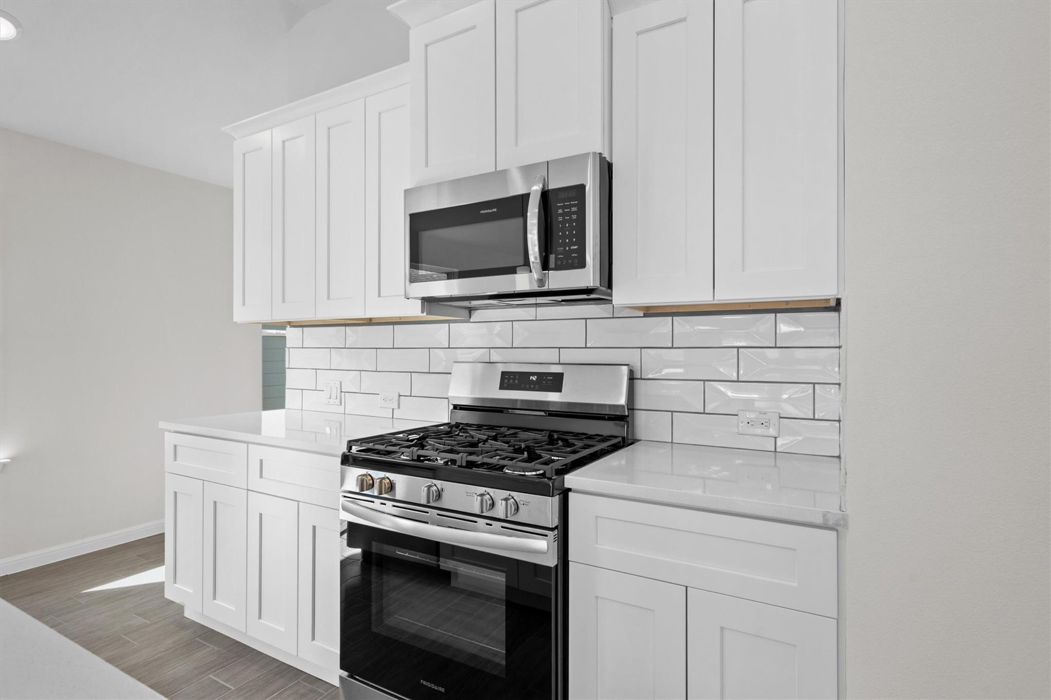 Kitchen with white shaker cabinets, subway tile backsplash, and stainless steel gas range.