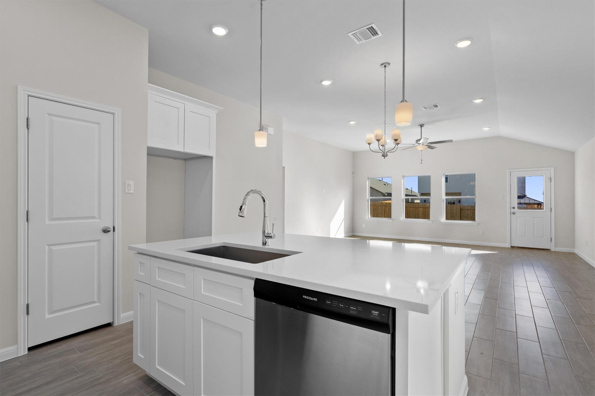 Open-plan kitchen with a large white island, sink, and dishwasher facing a bright living area.