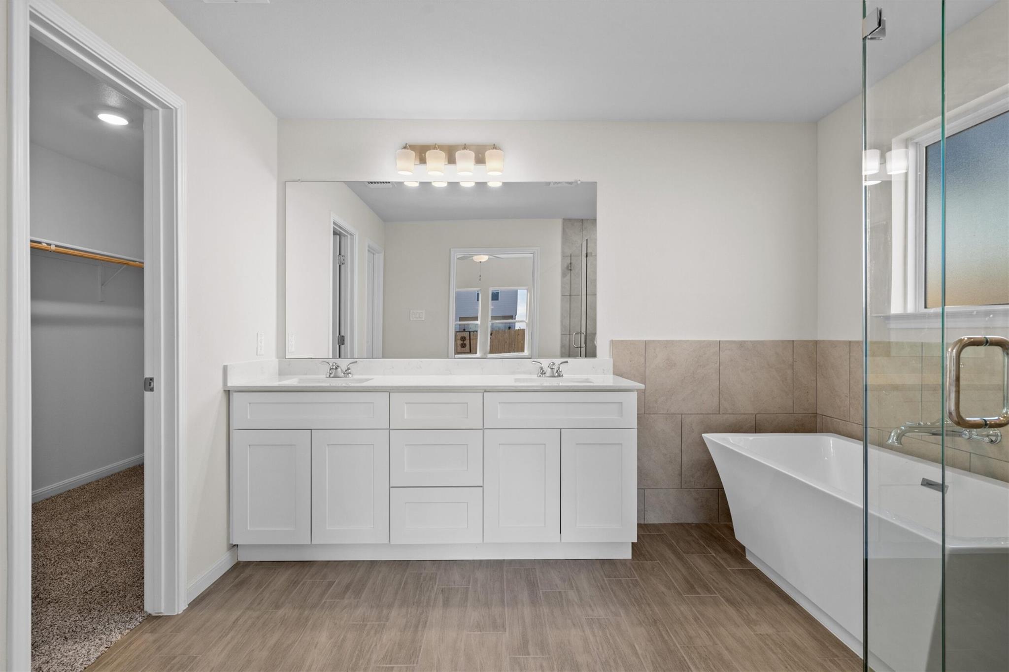 Bathroom with a white double vanity, freestanding soaking tub, and glass-enclosed shower.