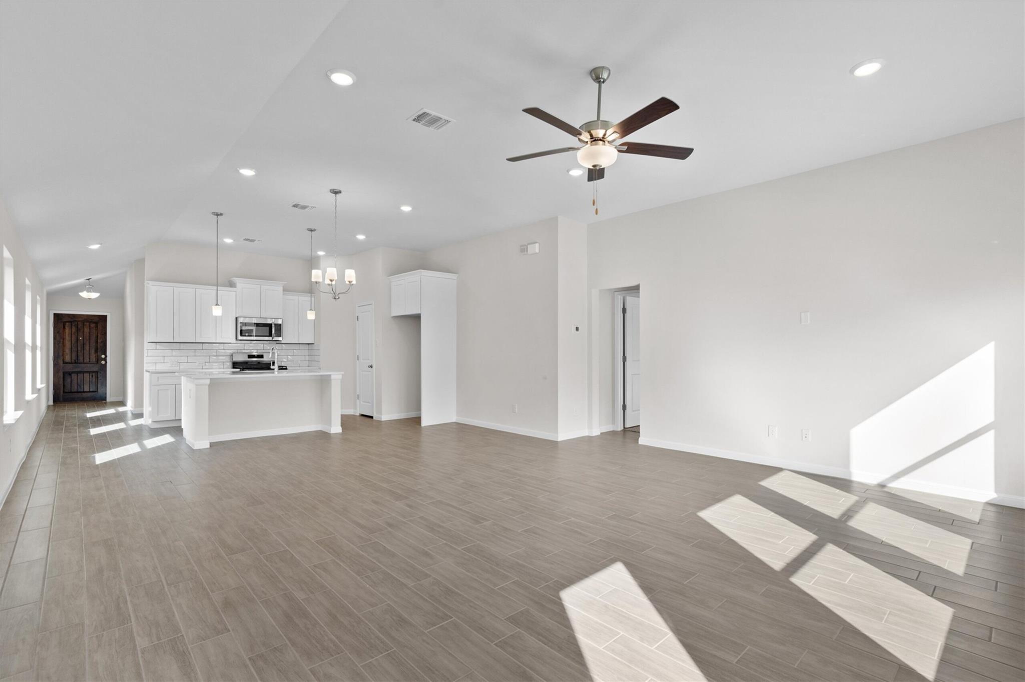 Open-plan kitchen and living area with white cabinets, gray tile floors, and bright sunlight.