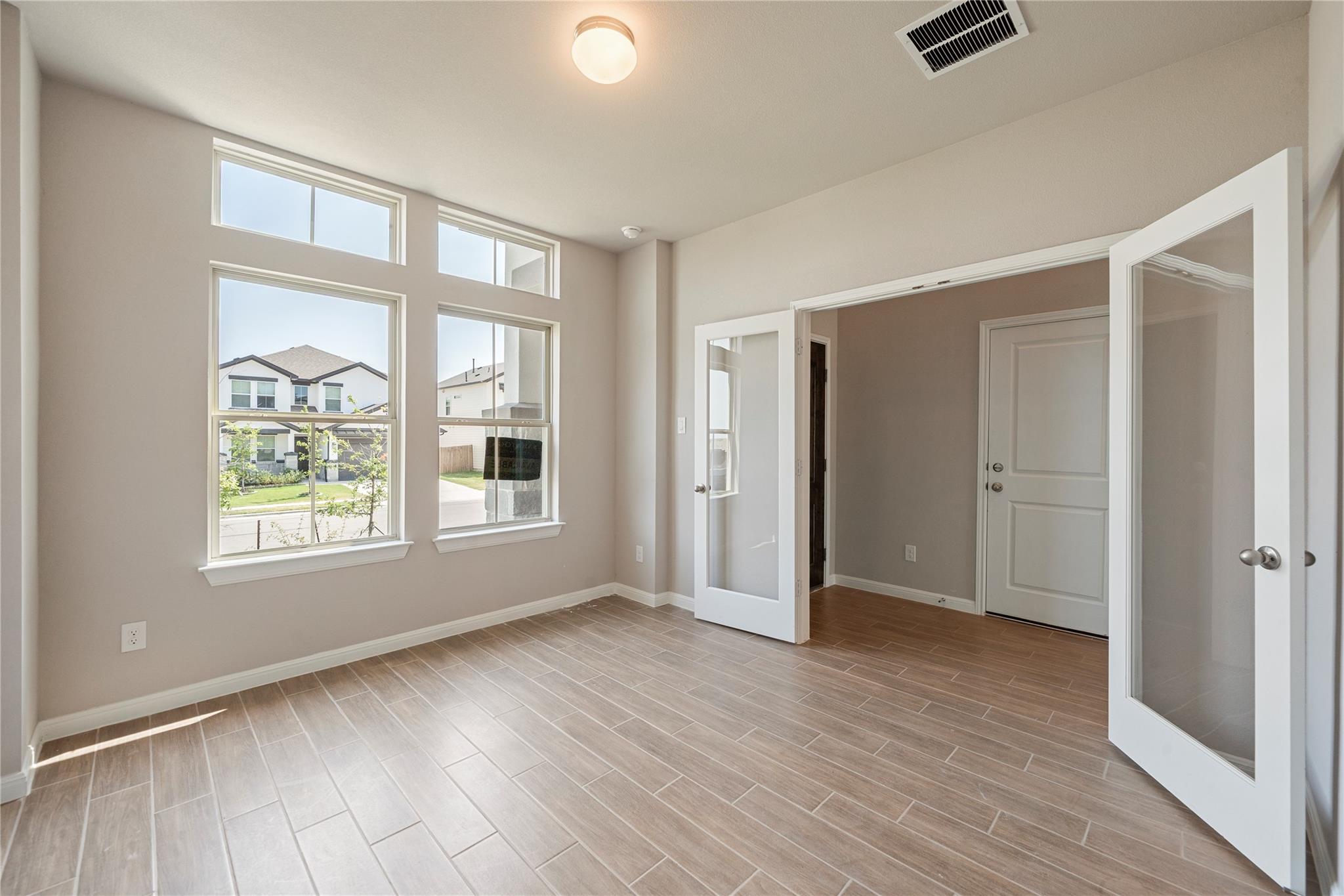 Empty room with wood-look tile floors, tall windows, and open glass-paneled doors.
