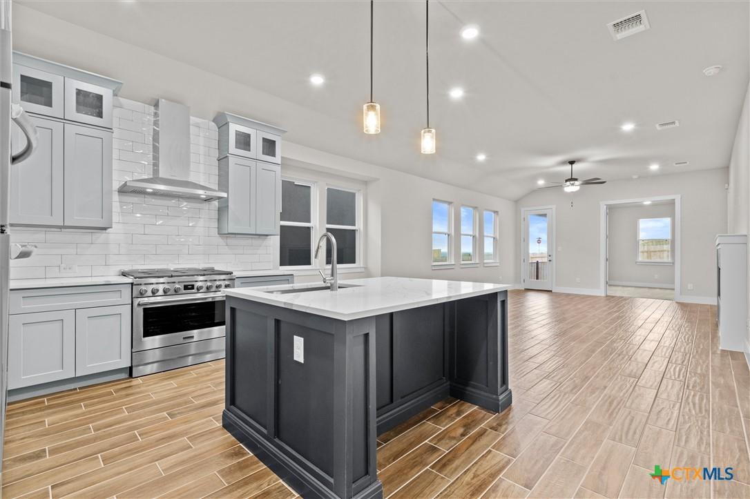 Open kitchen with a large dark island, stainless steel range, and wood-look tile flooring.