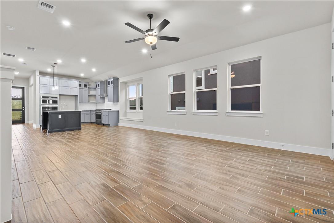 Open-plan kitchen and living area with gray cabinetry, a dark island, and wood-look tile flooring.