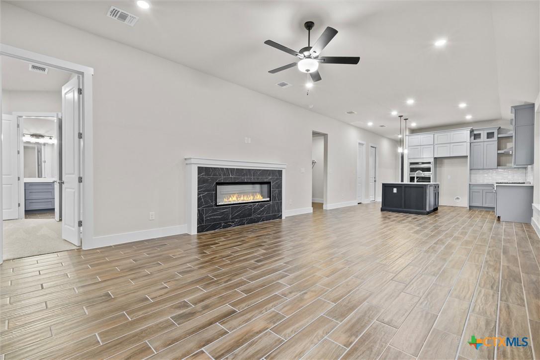 Open-plan living room and kitchen with a black marble fireplace, gray cabinets, and wood-look tile flooring.