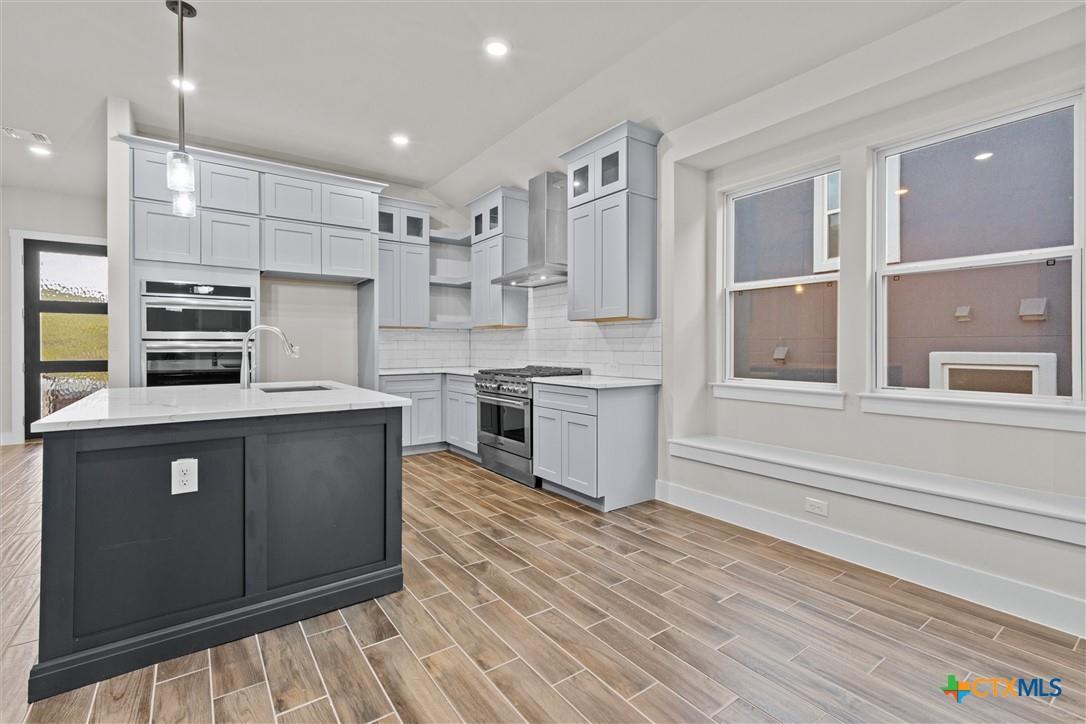 Modern kitchen with white cabinets, dark island, stainless steel appliances, and wood-look tile flooring.
