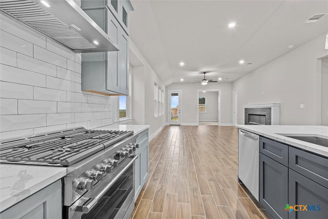 Open kitchen with stainless gas range, gray cabinetry, and a living room fireplace.