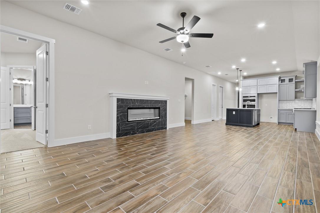 Vacant living room and kitchen with wood-look tile floors, a black marble fireplace, and a dark island.