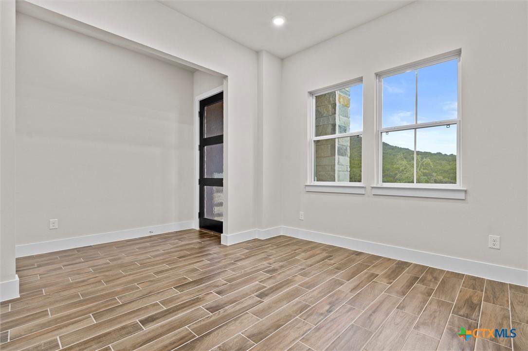 Empty room with wood-look tile floors, two windows overlooking green hills, and a black-framed glass door.
