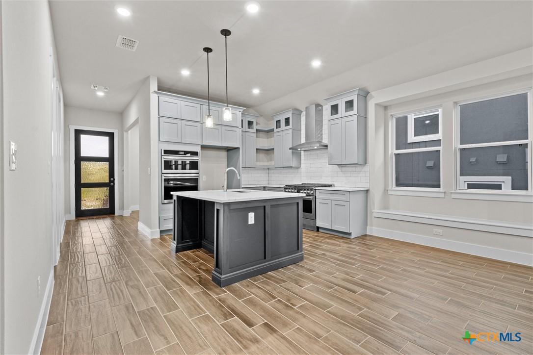 Vacant kitchen with a dark gray island, white cabinets, stainless steel appliances, and wood-look tile flooring.