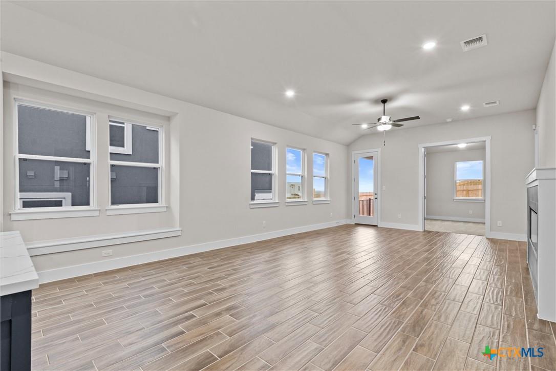 Vacant living room with wood-look tile floors, multiple windows, a patio door, and a partially visible fireplace.