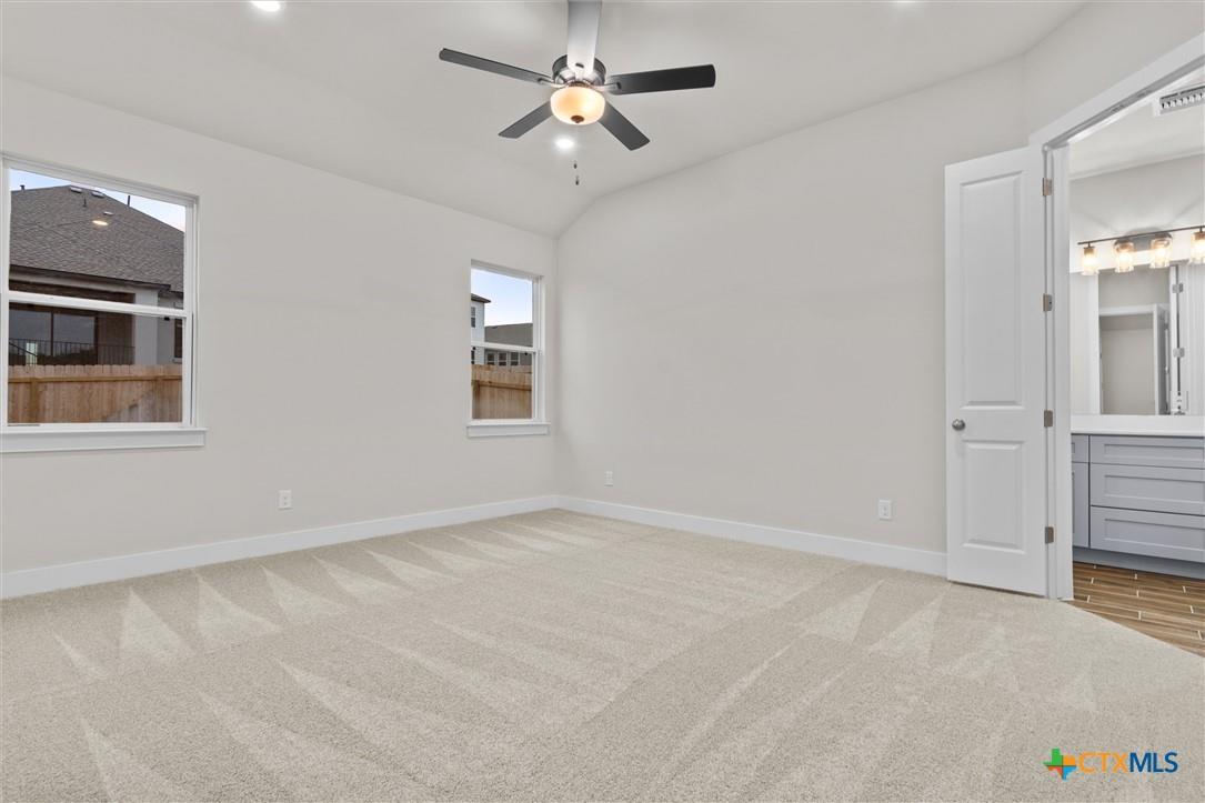 Vacant carpeted bedroom with two windows, a ceiling fan, and an open doorway to the bathroom.