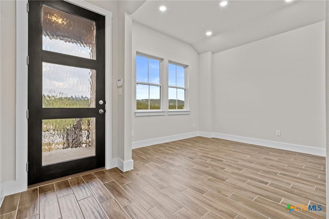 Empty entry with a black glass-paneled front door, two windows, and wood-look tile flooring.