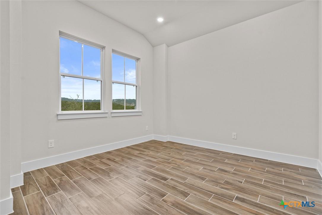 Empty room with two tall windows and brown wood-look tile flooring.