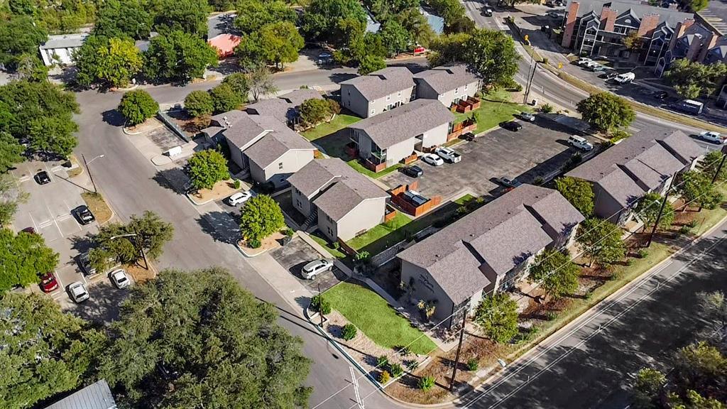 Aerial view of a condominium complex with low-rise buildings, parking areas, and mature trees.