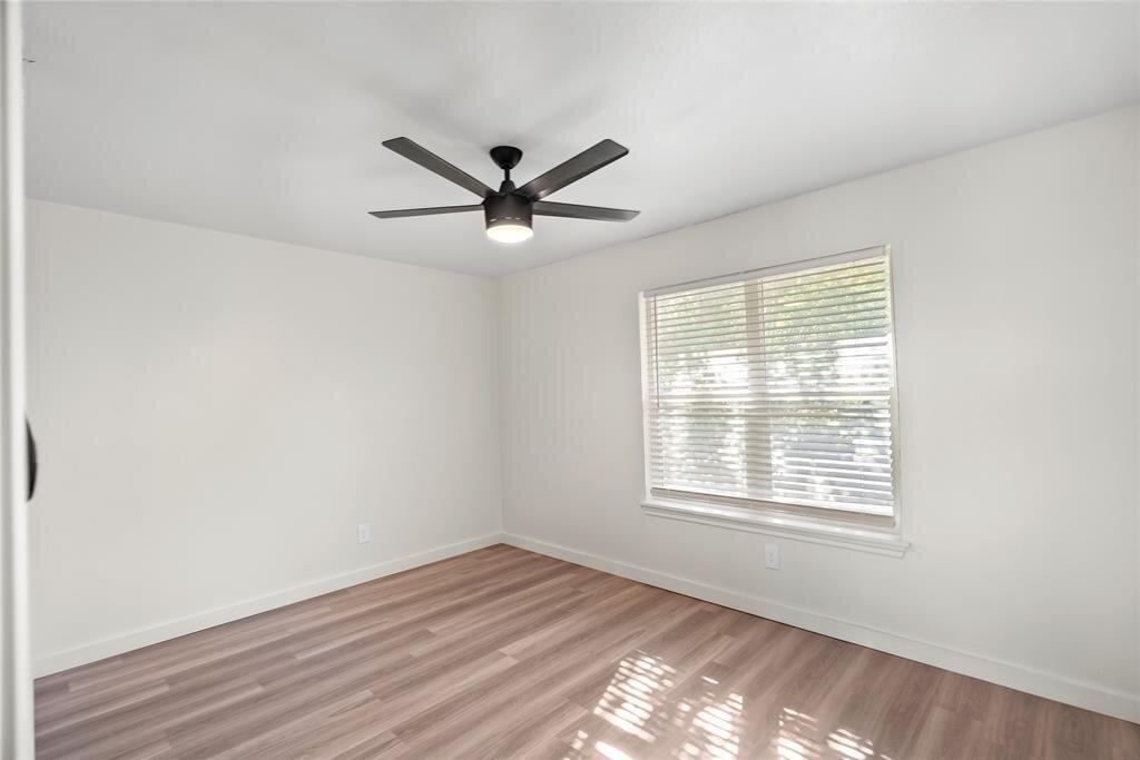 Empty bedroom with wood-look flooring, a ceiling fan, and a window with blinds.