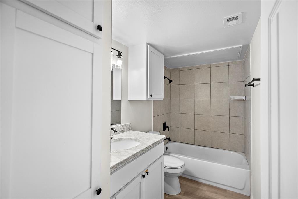 Bathroom with a white vanity, toilet, and bathtub surrounded by large beige tiles.