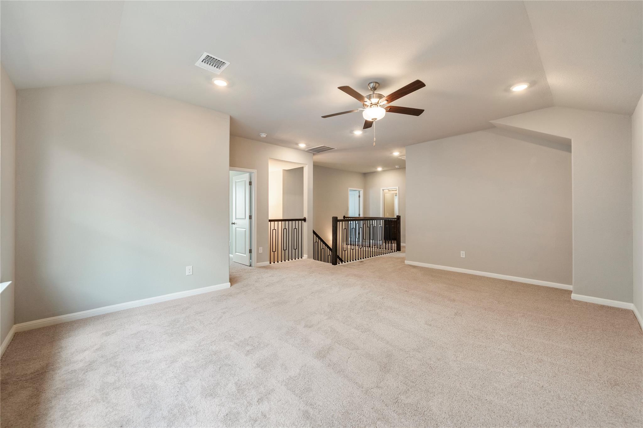 Empty carpeted upstairs loft with a ceiling fan and dark railing around the stairwell.