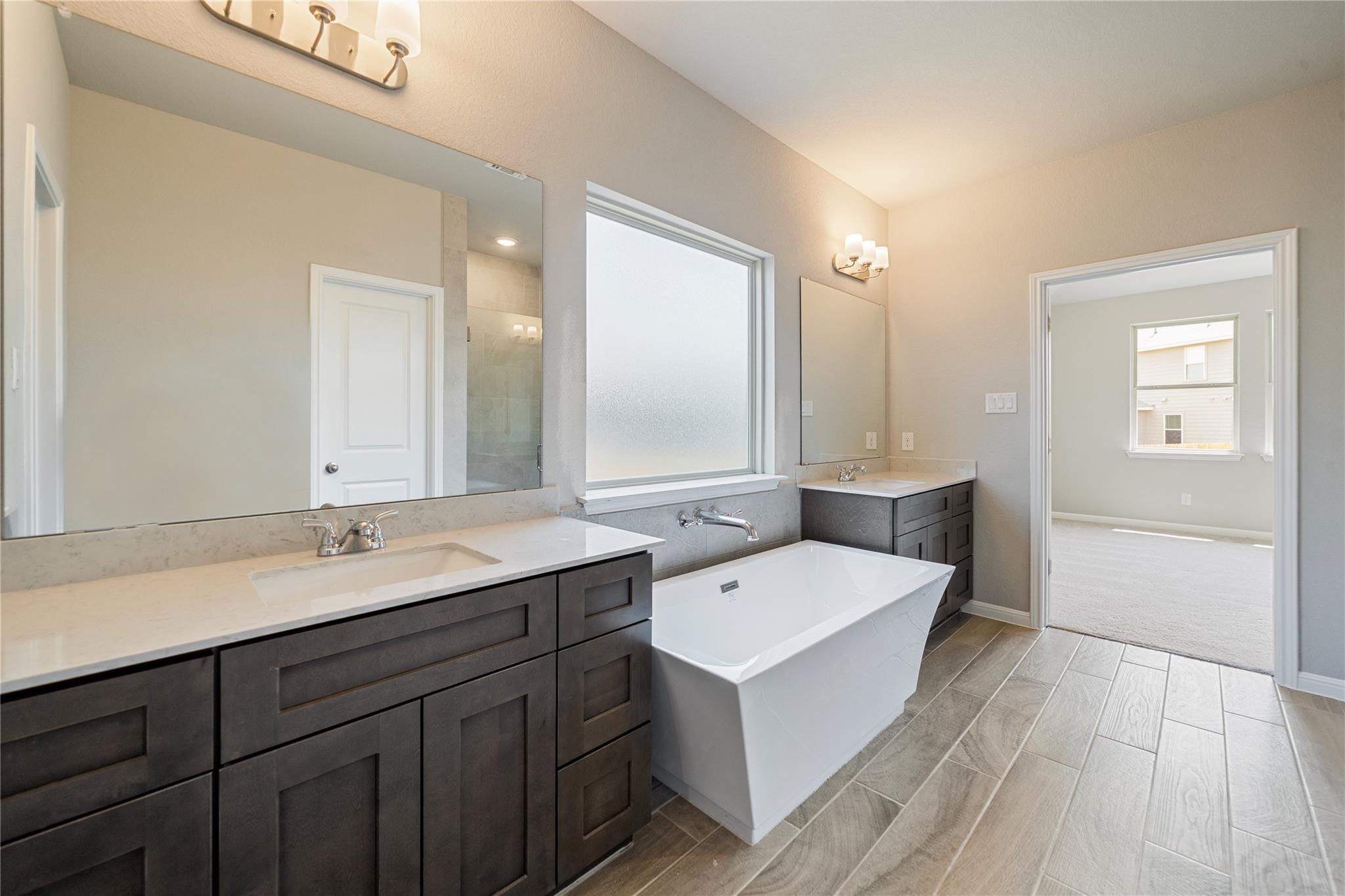 Primary bathroom with a freestanding soaking tub, dark double vanities, and gray wood-look tile flooring.