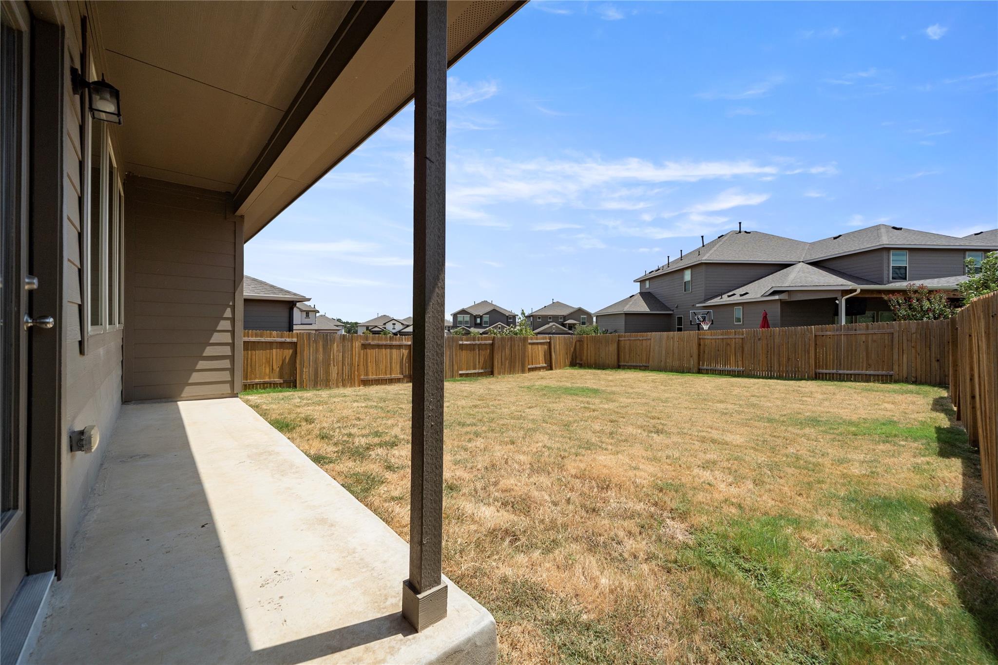 Fenced backyard with a covered concrete patio and dry, patchy lawn.