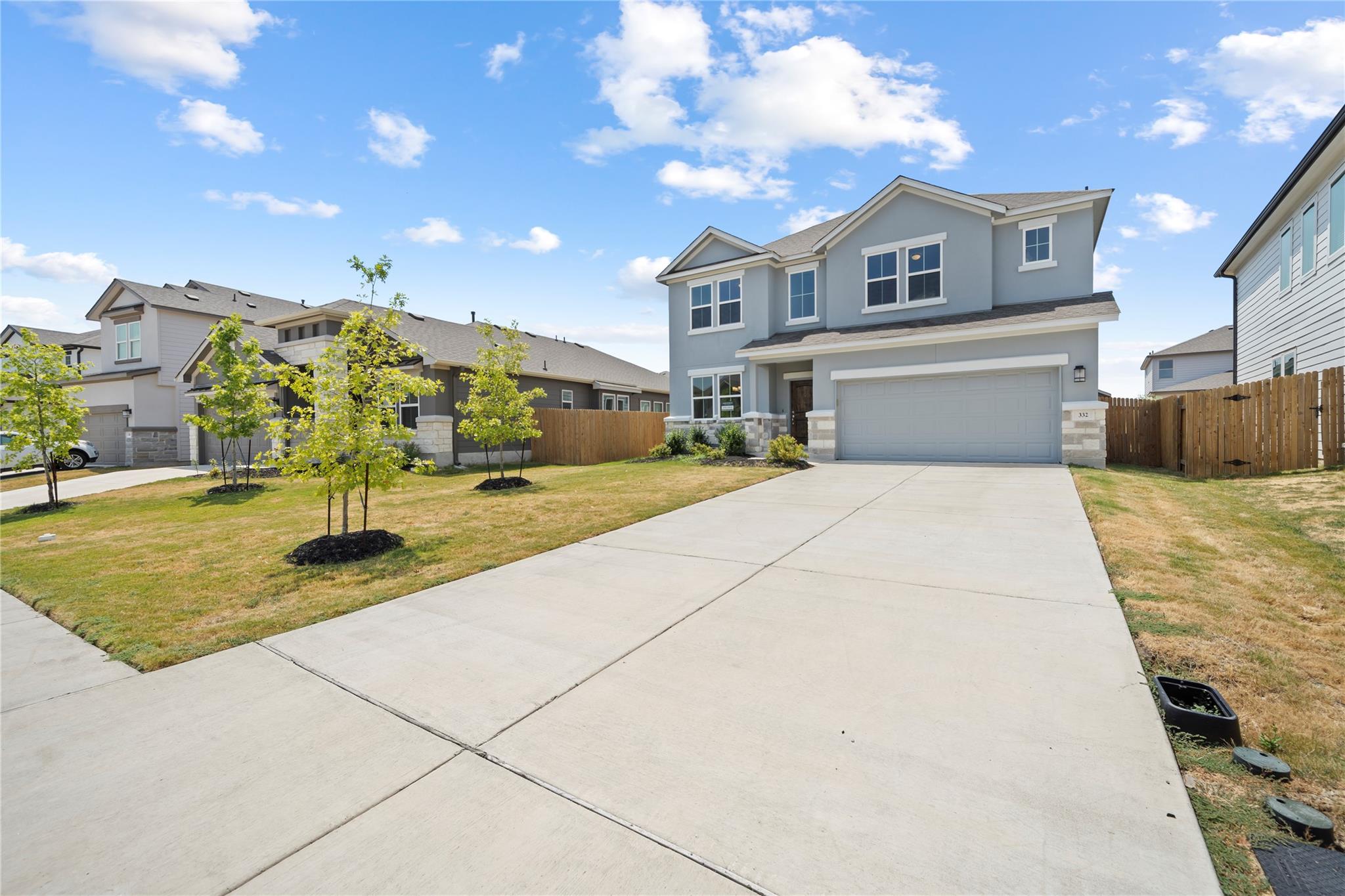 Two-story gray home with a two-car garage, wide driveway, and young trees in the front yard.