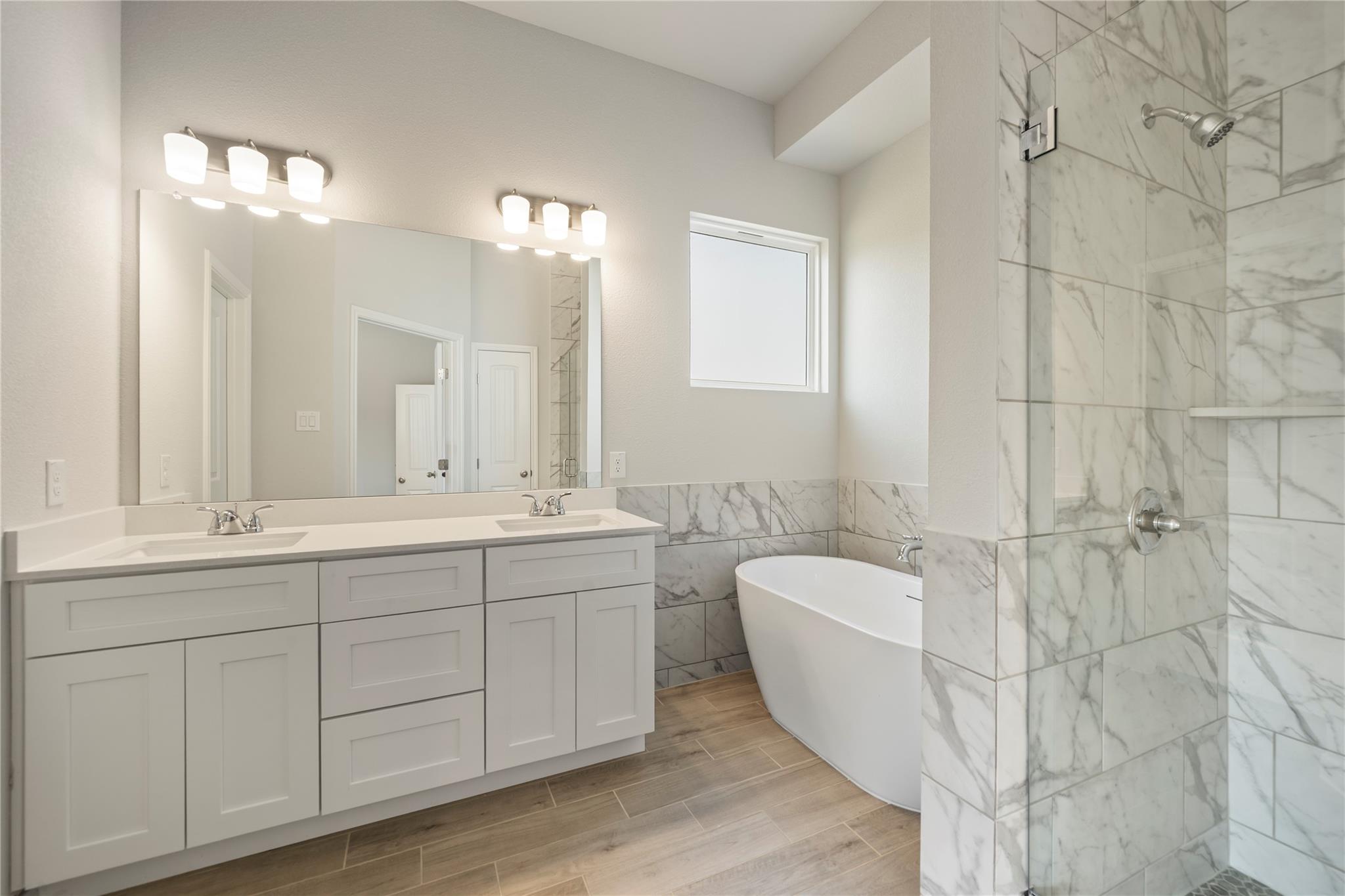 Bathroom with a double vanity, freestanding tub, and marble-look tiled shower.