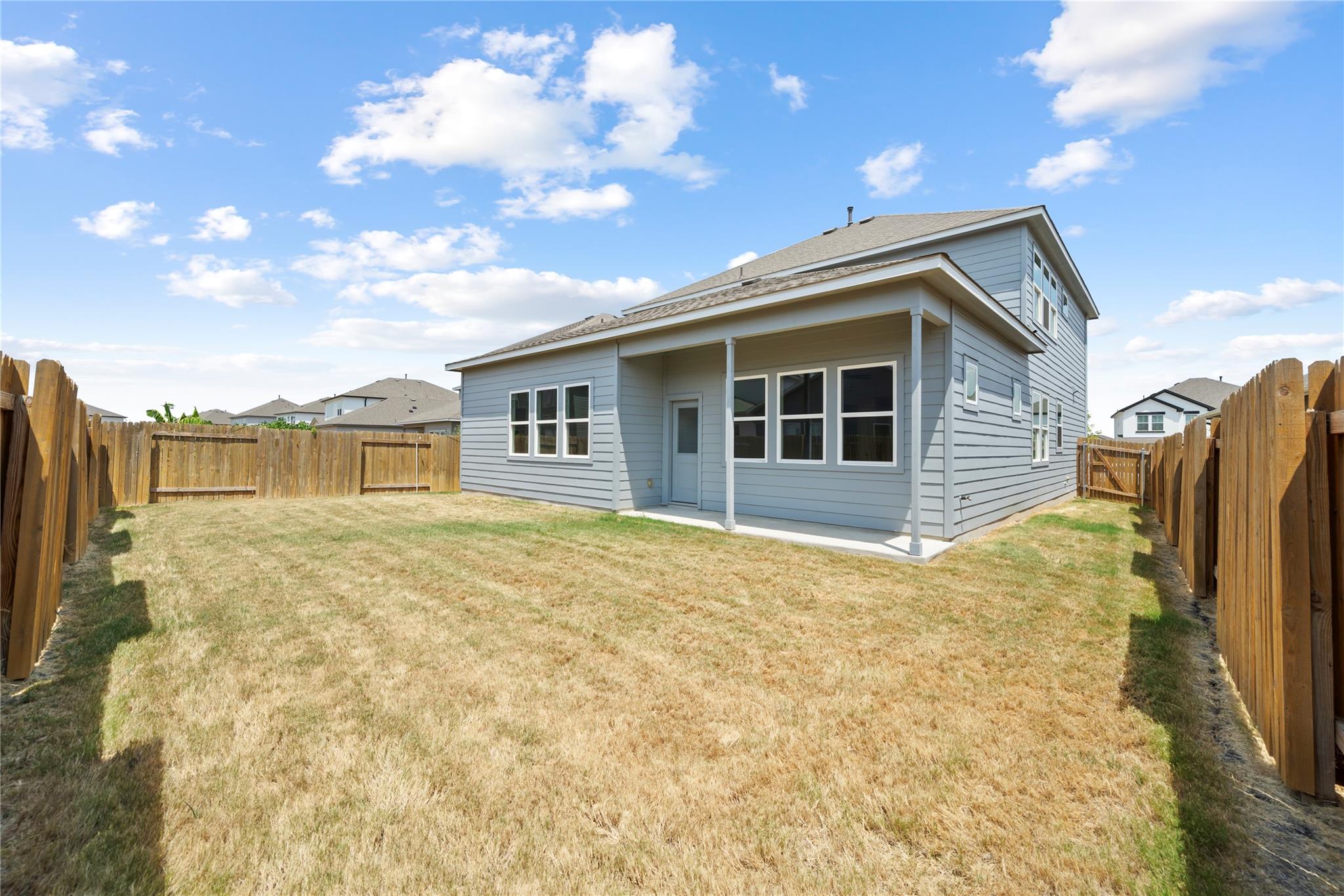 Rear of a gray two-story home with a covered patio and fenced backyard.