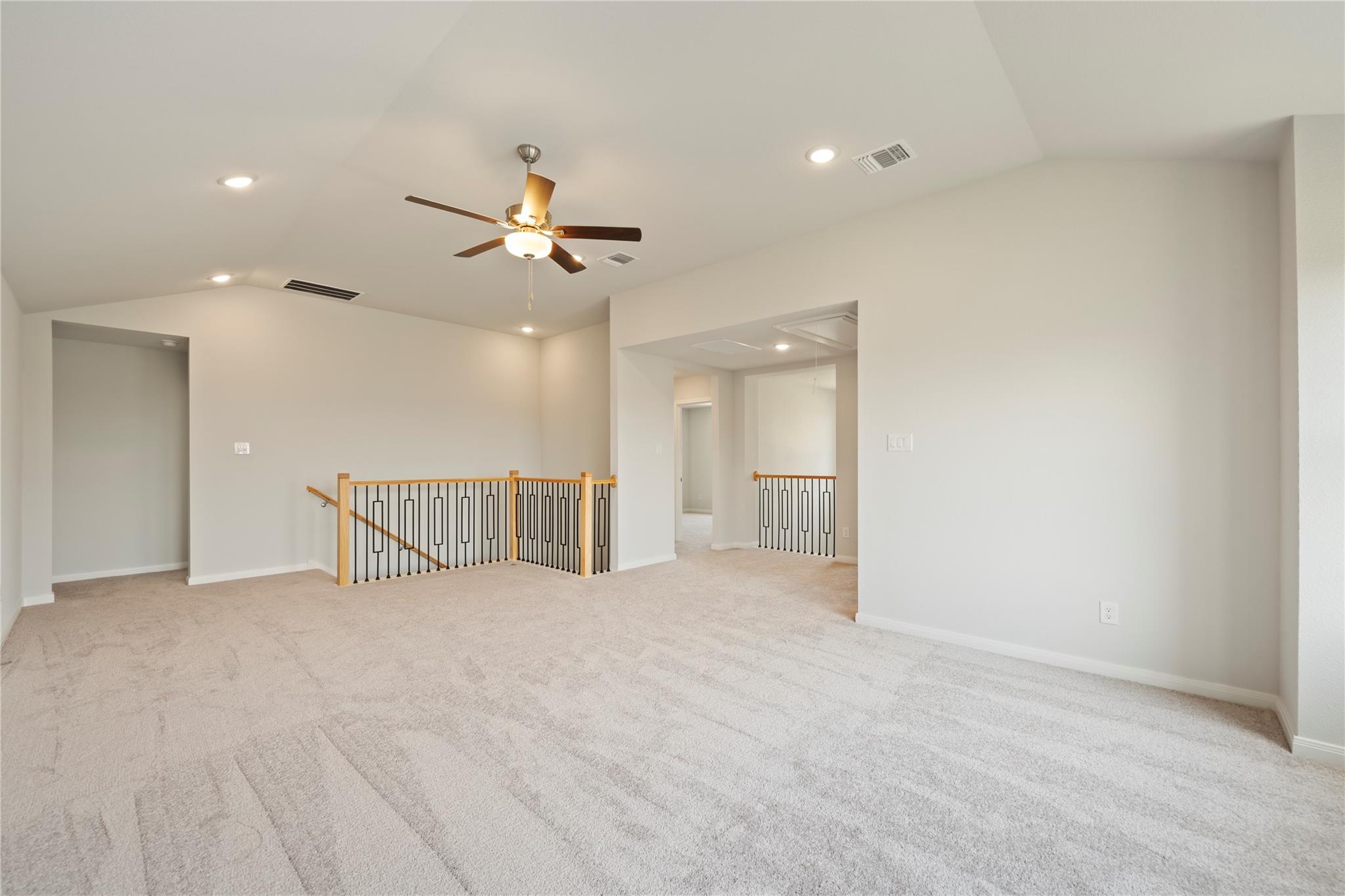 Carpeted upstairs loft with a ceiling fan and wood-and-metal stair railings.