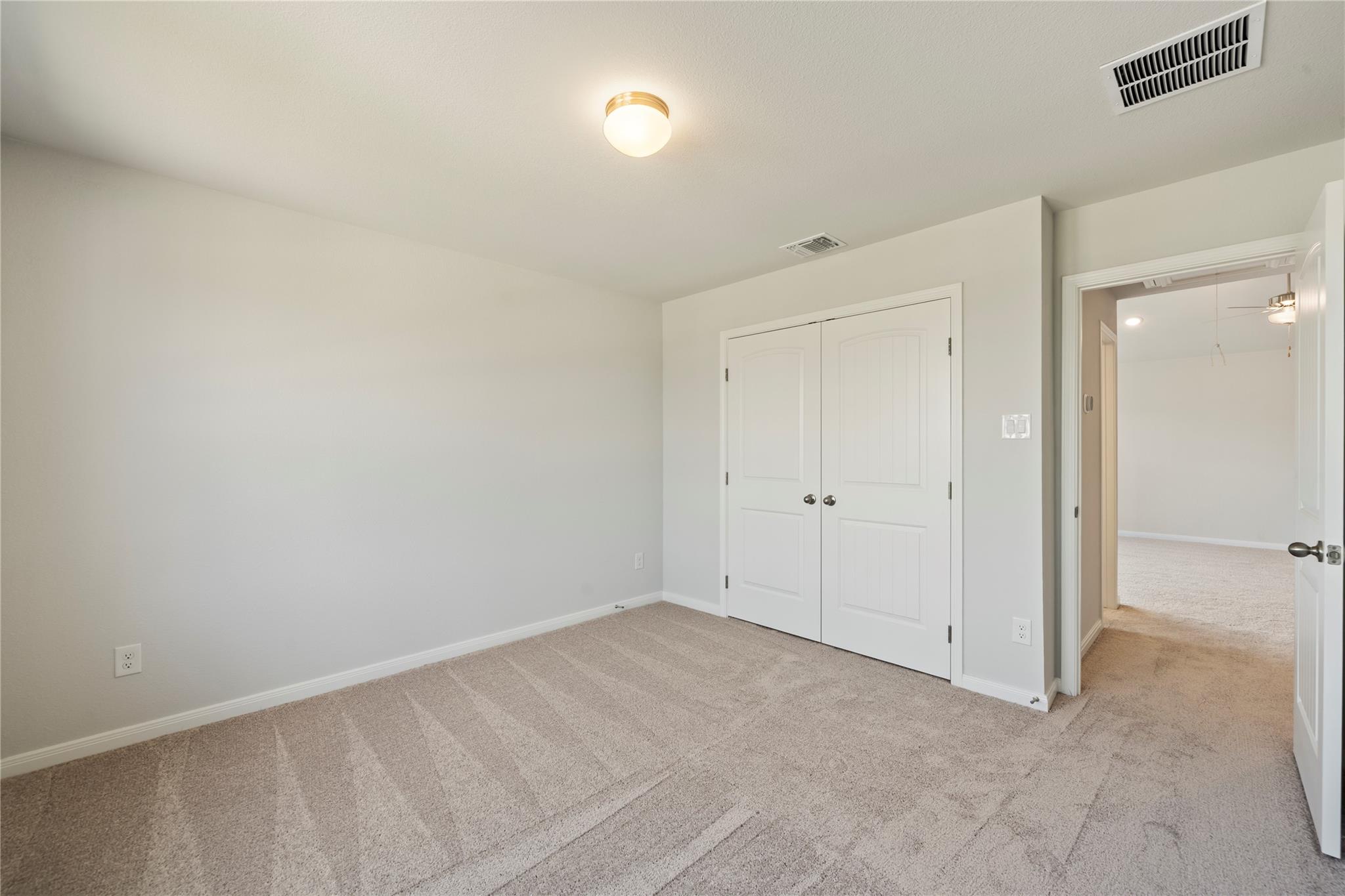 Empty carpeted bedroom with double closet doors and an open doorway to another room.