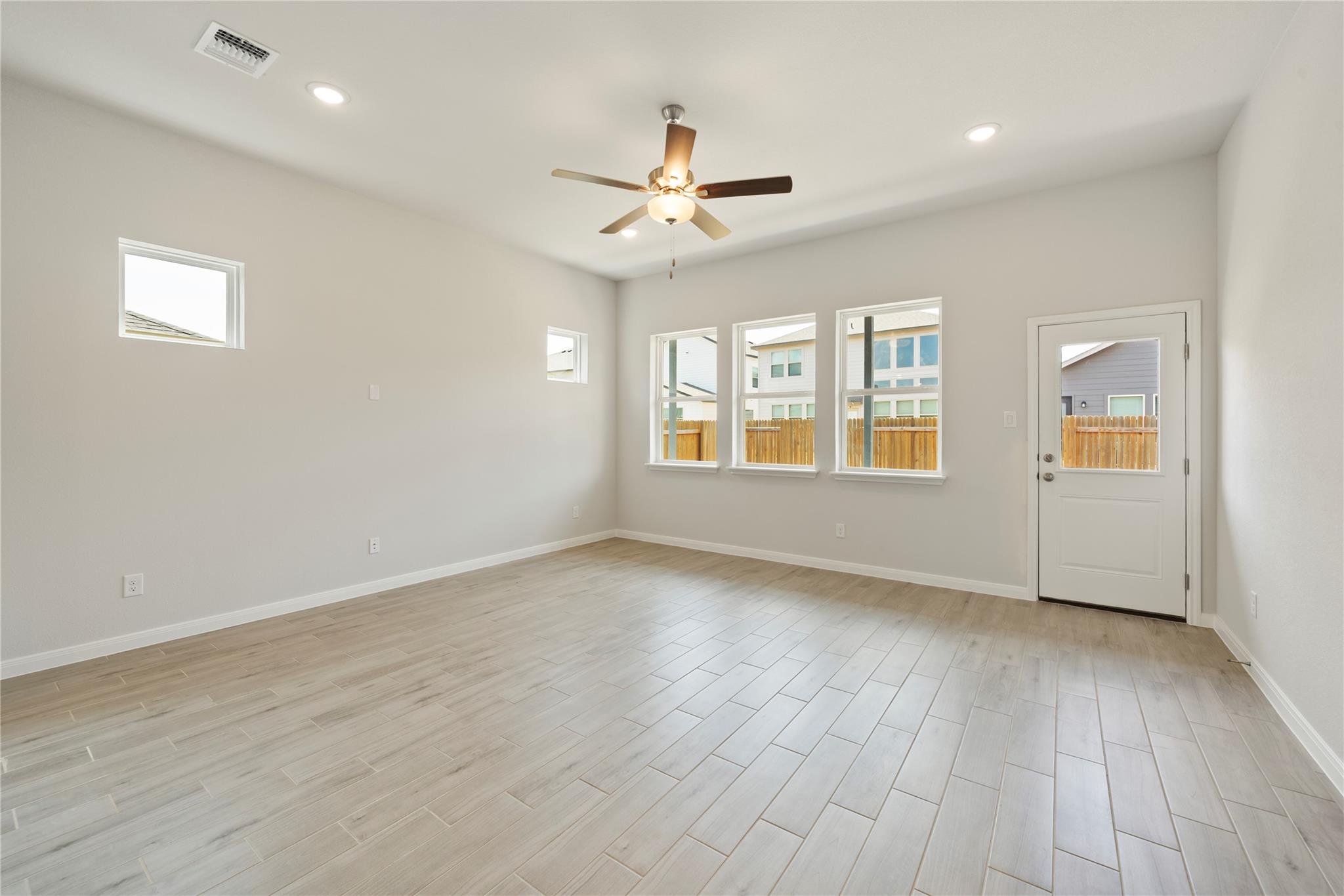 Vacant room with wood-look tile floors, a ceiling fan, three windows, and a glass-panel door.