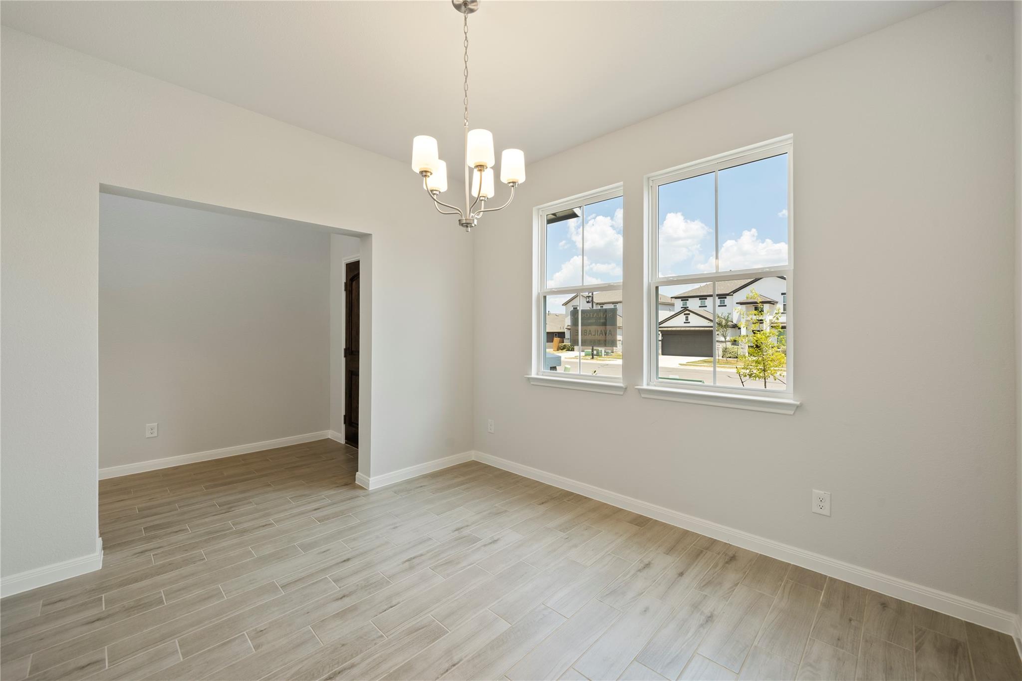 Empty dining room with tile flooring, a chandelier, and two windows overlooking neighboring homes.