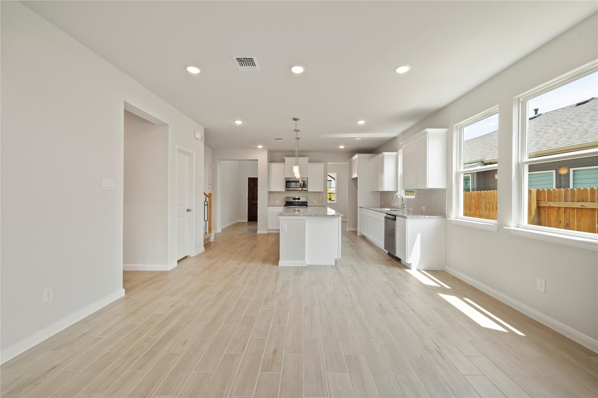 Vacant kitchen with a white island, stainless steel appliances, and large windows.
