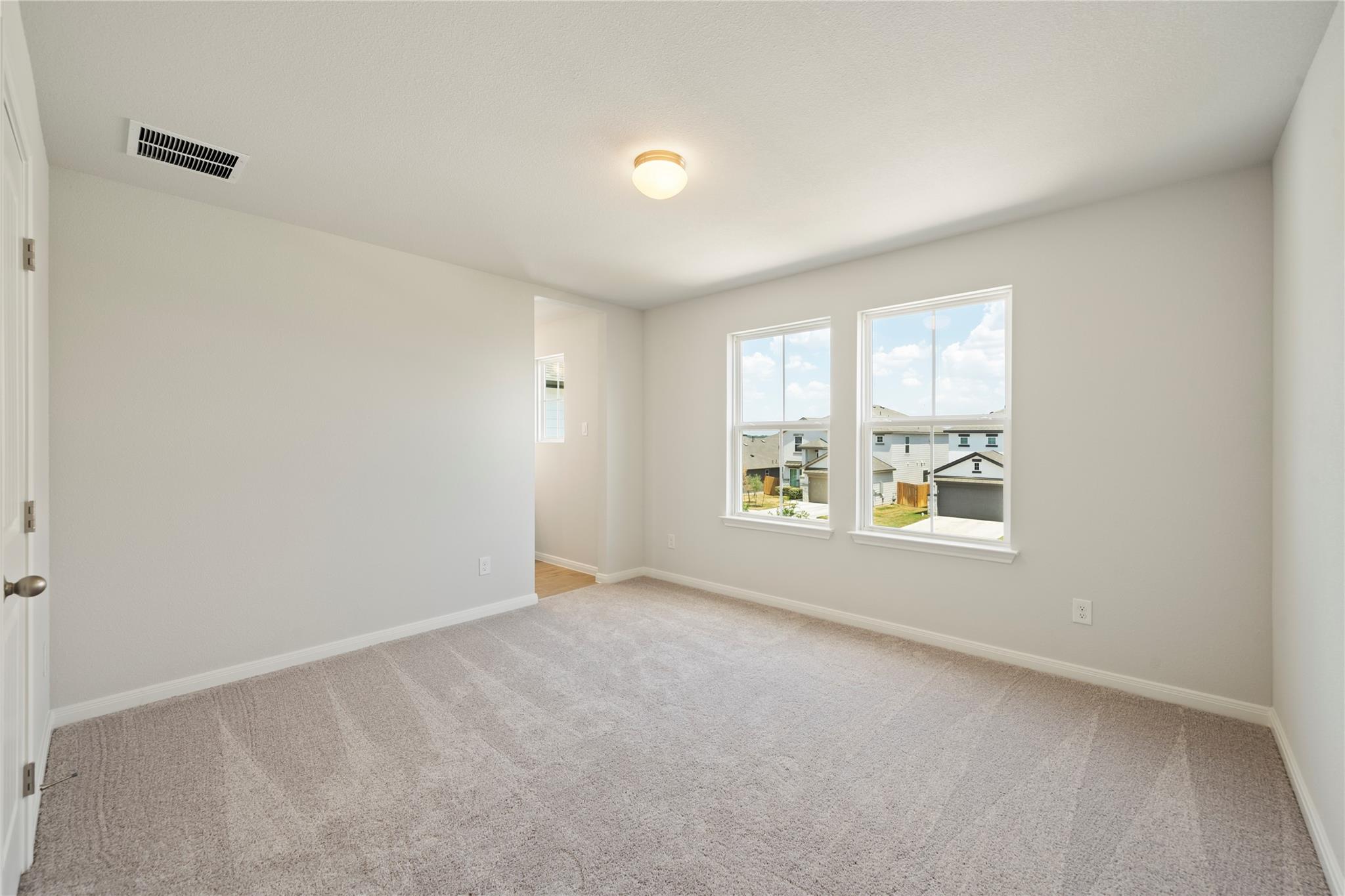Empty carpeted bedroom with two windows overlooking neighboring homes.