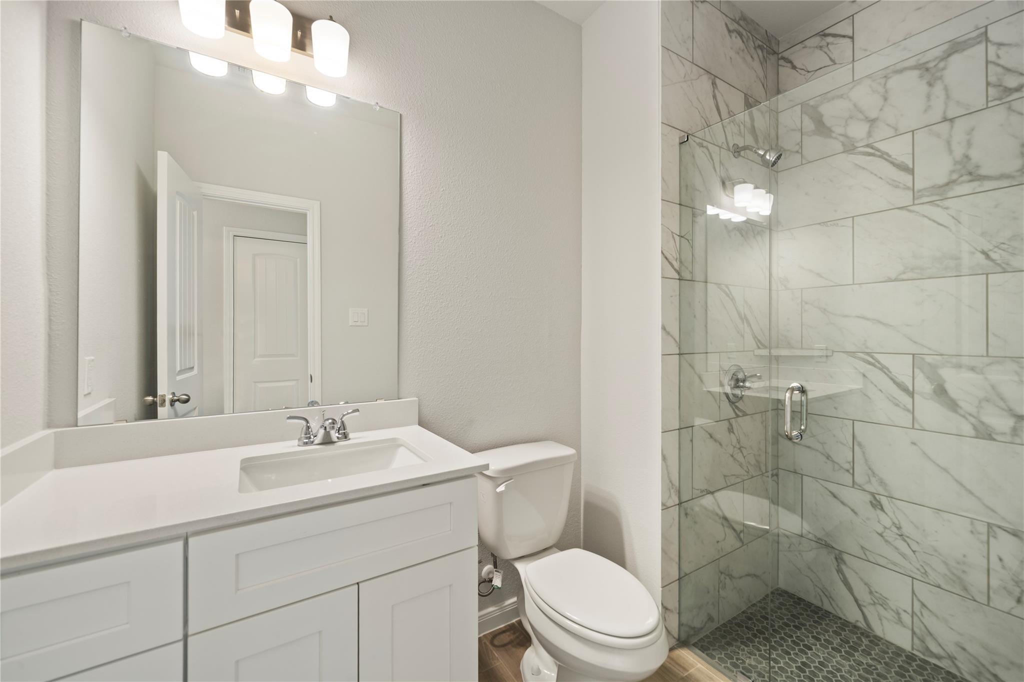 Bathroom with a white vanity and a glass shower lined with marble-look tile.