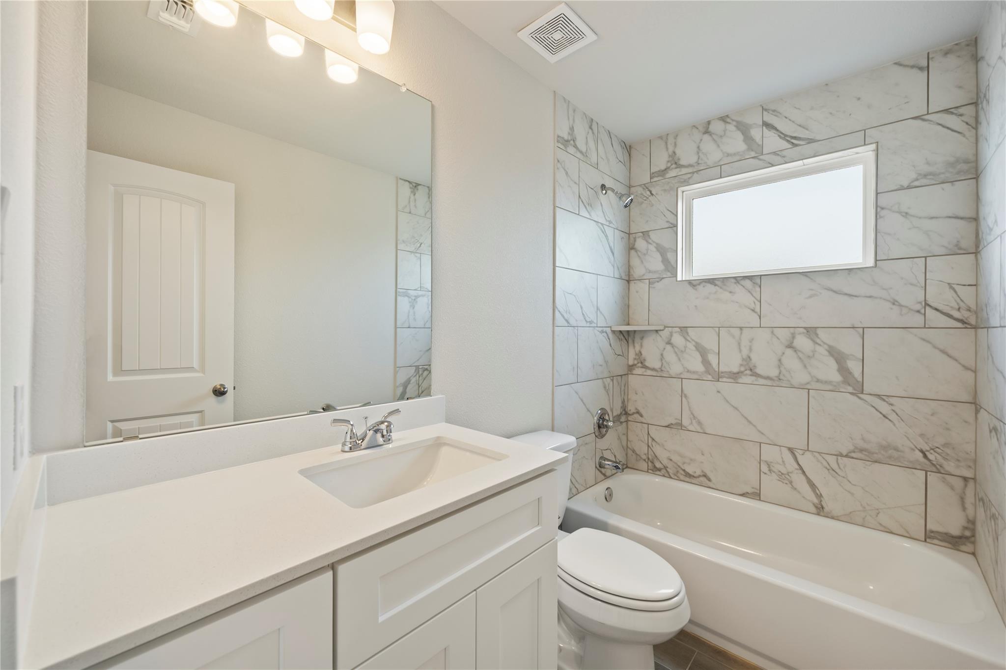 Bathroom with white vanity, toilet, and bathtub surrounded by marble-look tile.