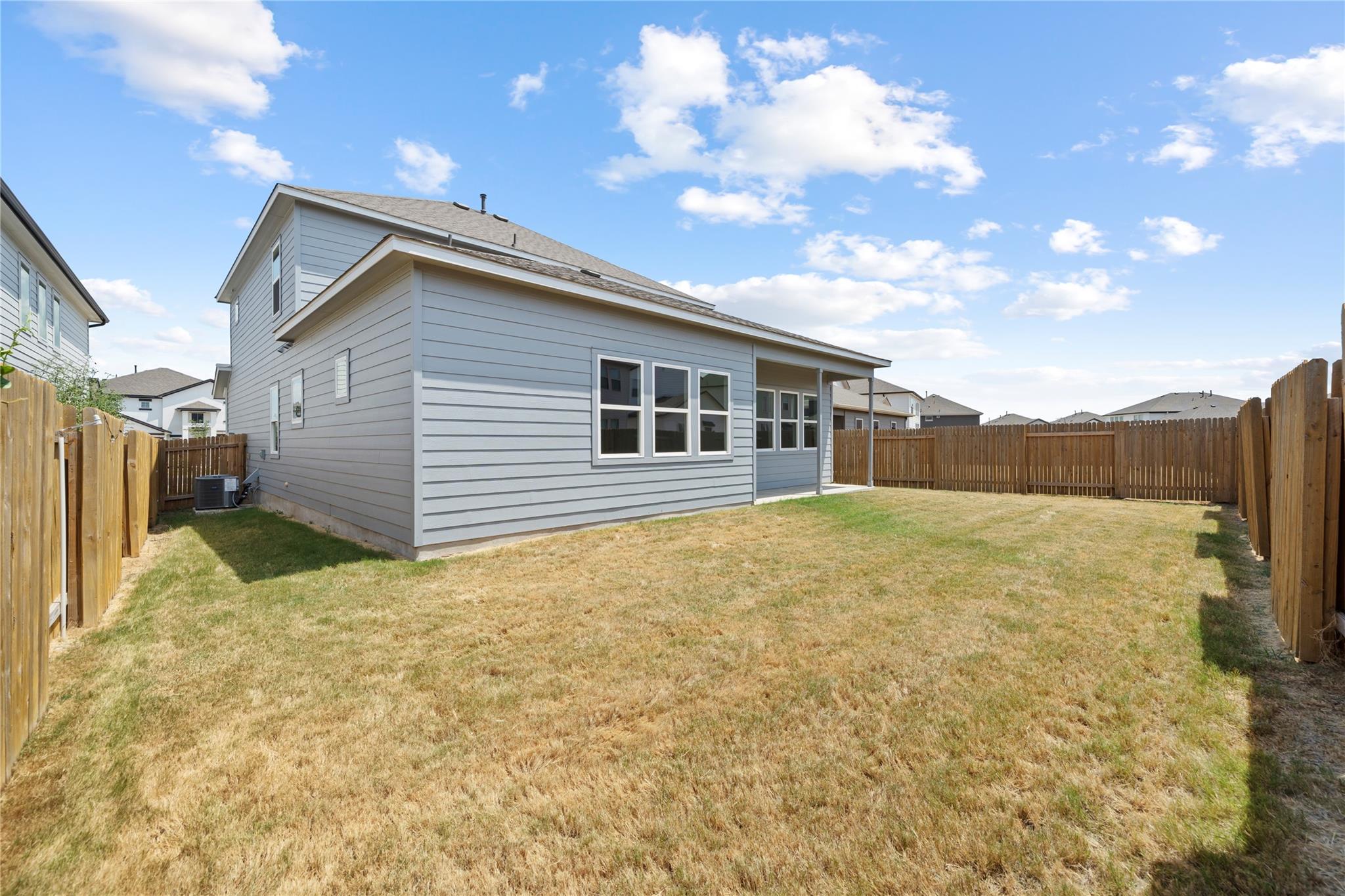 Gray two-story home with a covered patio and fenced backyard with a broad, dry lawn.