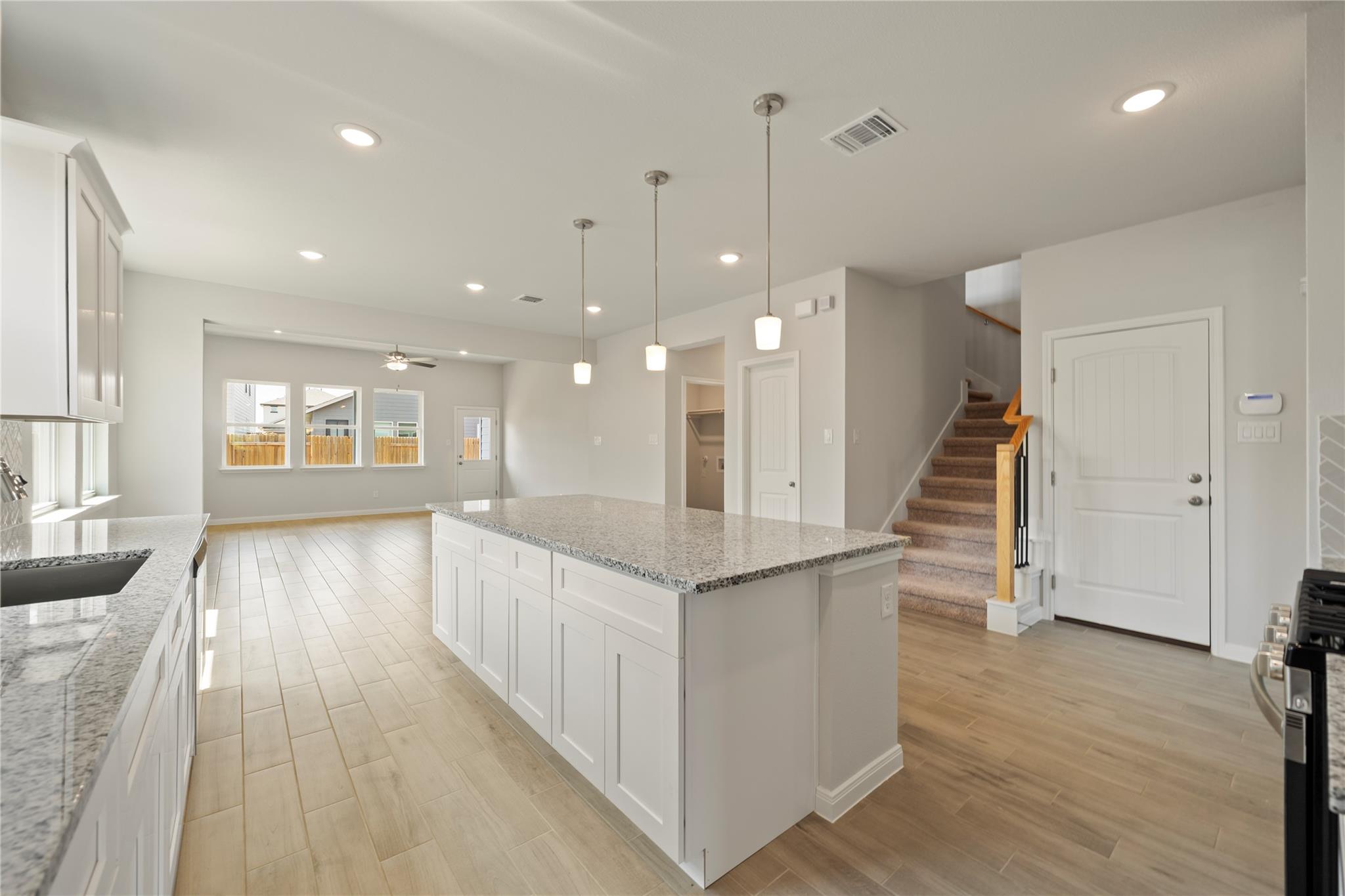 Open-plan kitchen with a large granite island, white cabinetry, and stairs beside the front door.