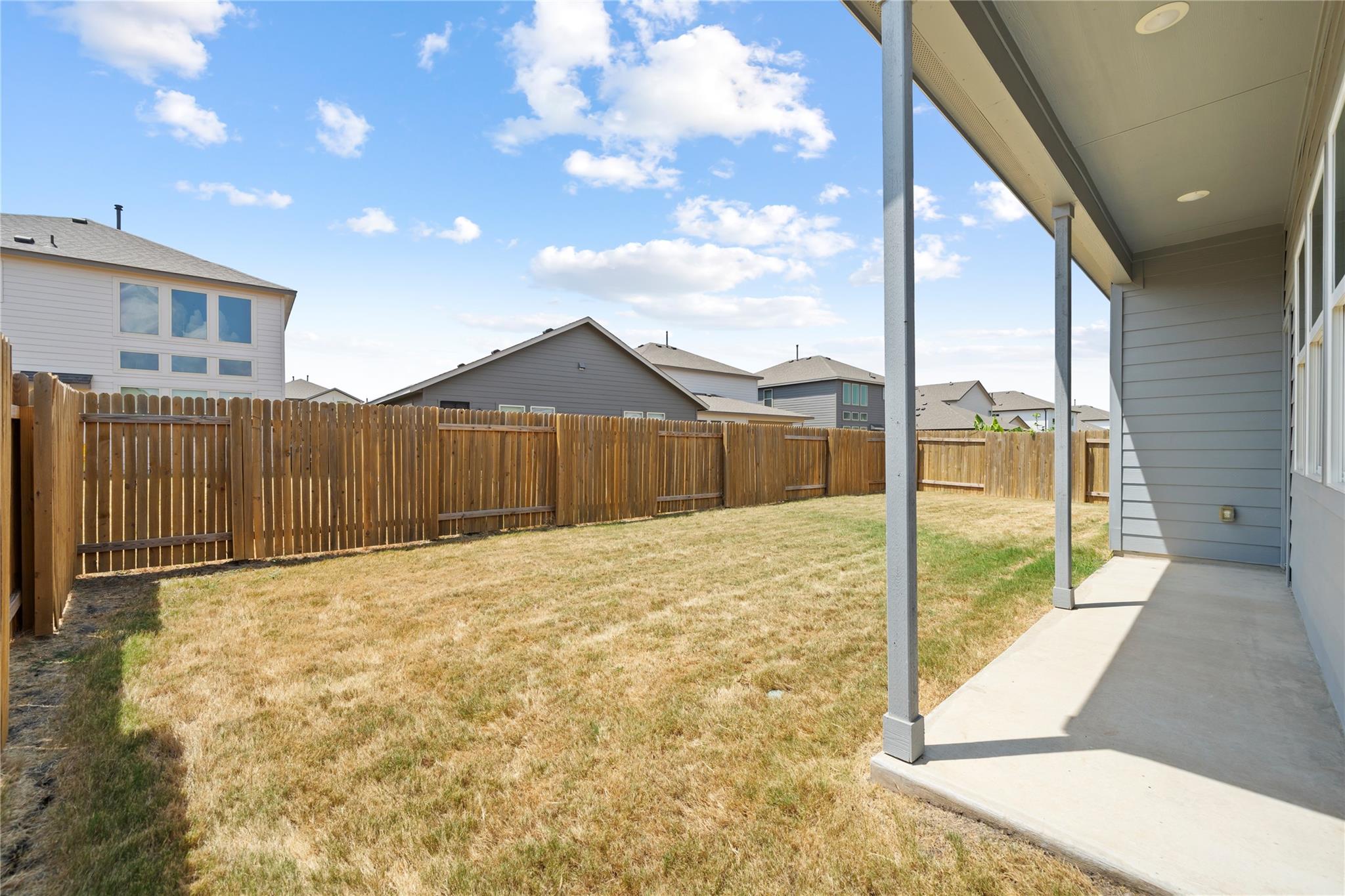Fenced backyard with a covered patio and patchy lawn.