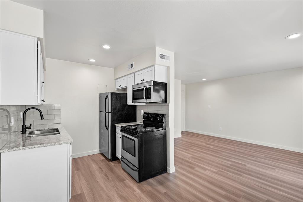 Vacant kitchen opening to an empty living area, with black appliances and wood-look floors.