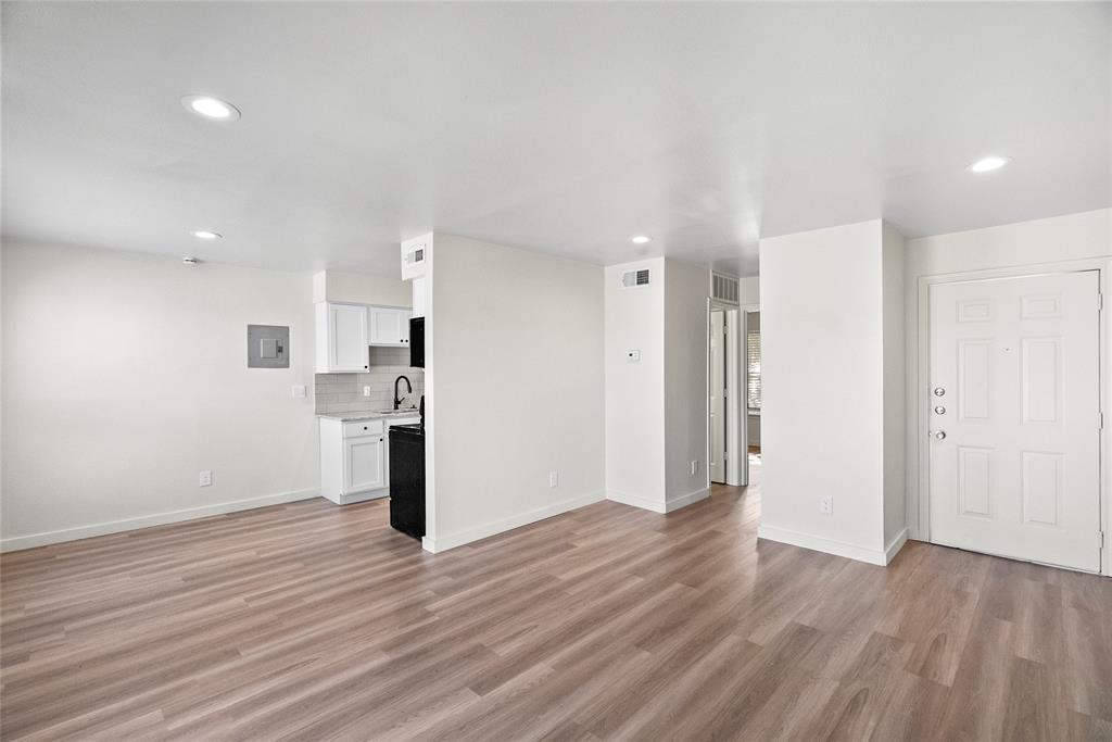 Empty open-plan living area with wood-look floors, recessed lights, and a compact kitchen.
