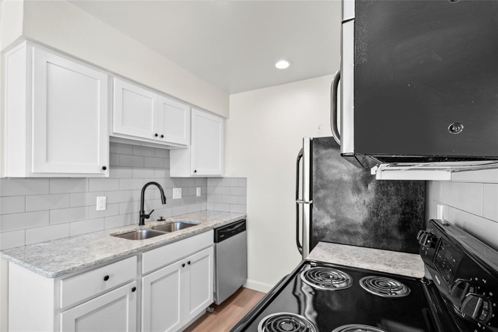 Kitchen with white cabinets, gray tile backsplash, stone counters, and a black electric range.