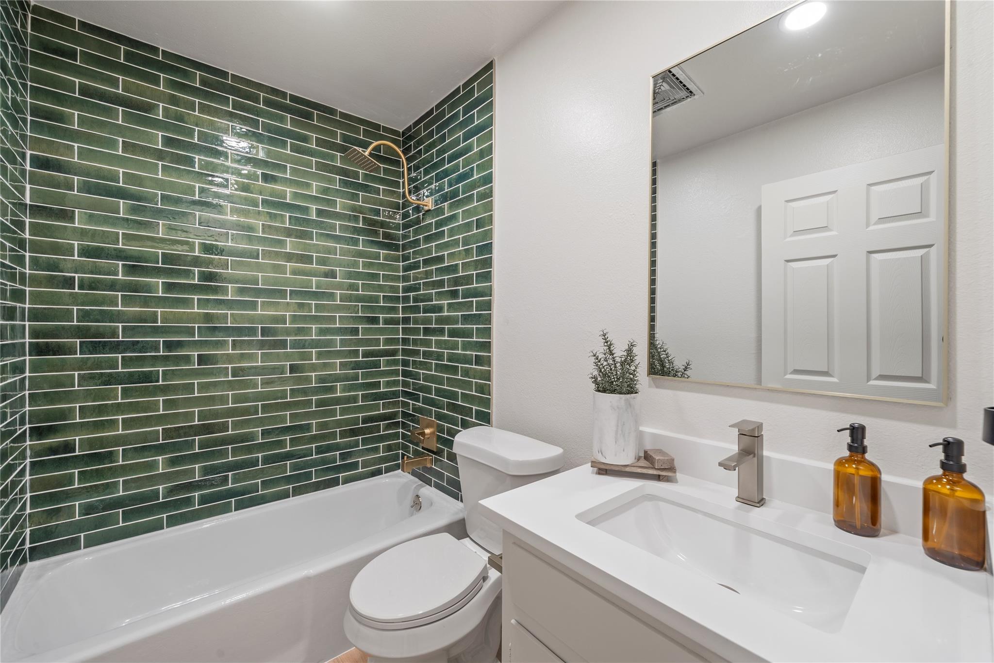 Bathroom with dark green subway tile, a white tub, and a vanity with a large mirror.