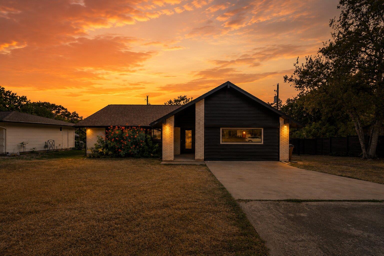 Single-story dark-sided house with brick accents and a driveway beneath an orange sunset sky.