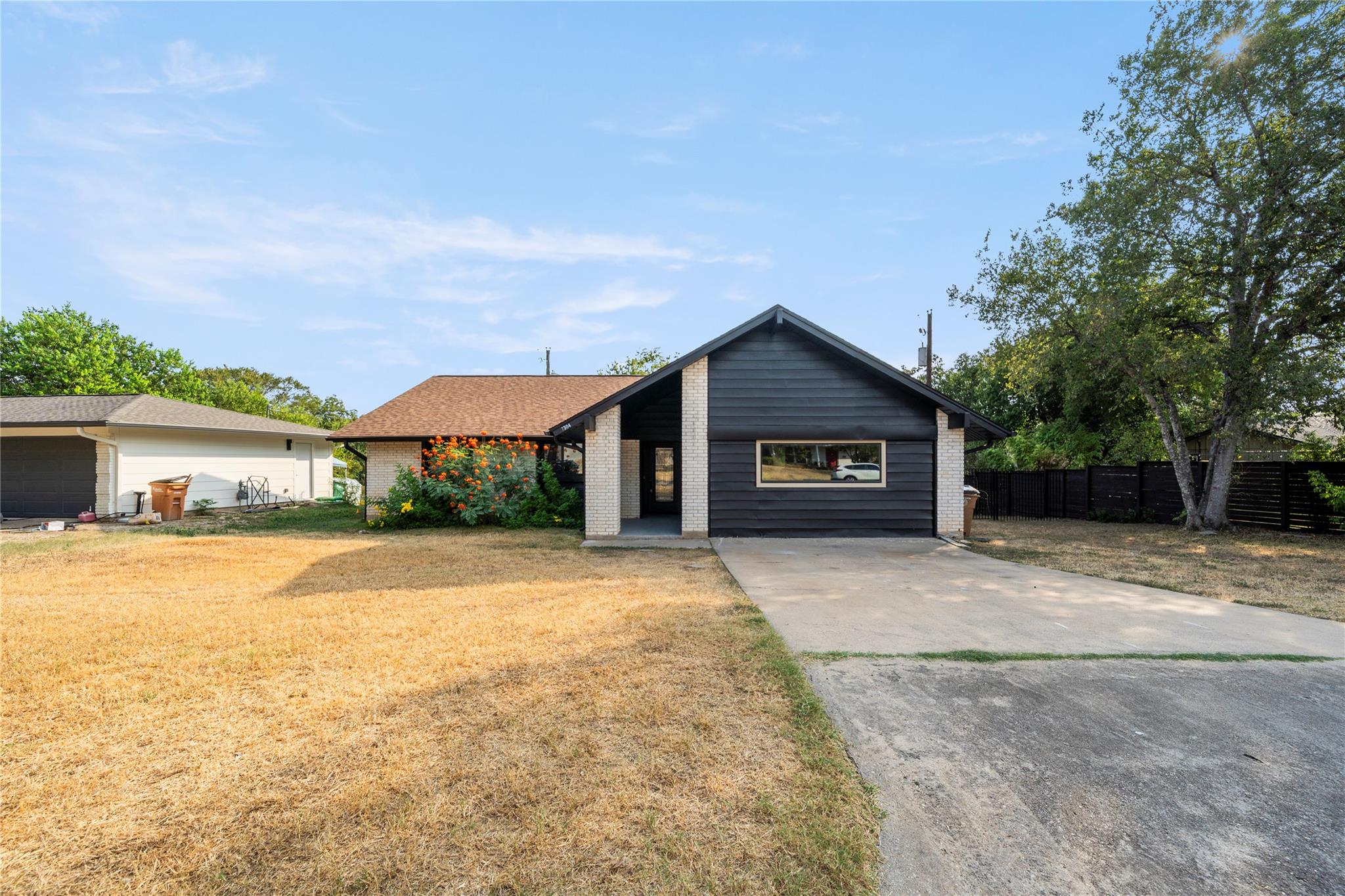 Single-story home with dark siding, light brick accents, a concrete driveway, and a dry front lawn.